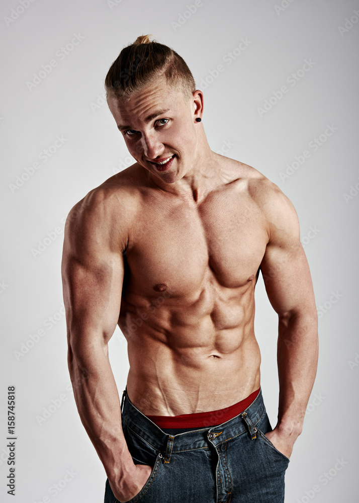 Young handsome guy with naked sexy torso posing in studio over gray background. 