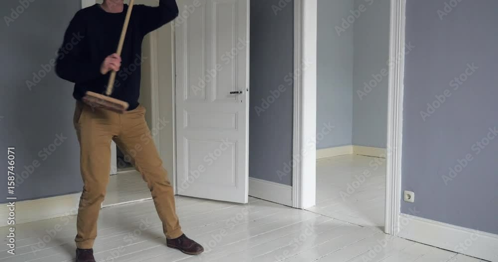 A man sings. dances, and twirls his way around an empty room with a sweeper in hand. A man sings. dances, and twirls his way around an empty room with a sweeper in hand.