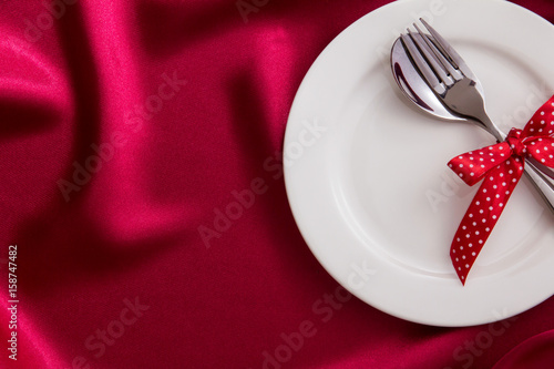  White empty plate with fork and spoon on red silk fabric for dinner setting