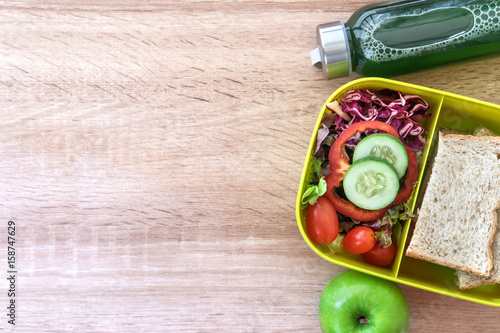 The Healthy Lunch box with grain bread and green vegetable and fruit juice bottle on wooden background ,Healthy eating clean food habits for diet concept , top view and overhead shot