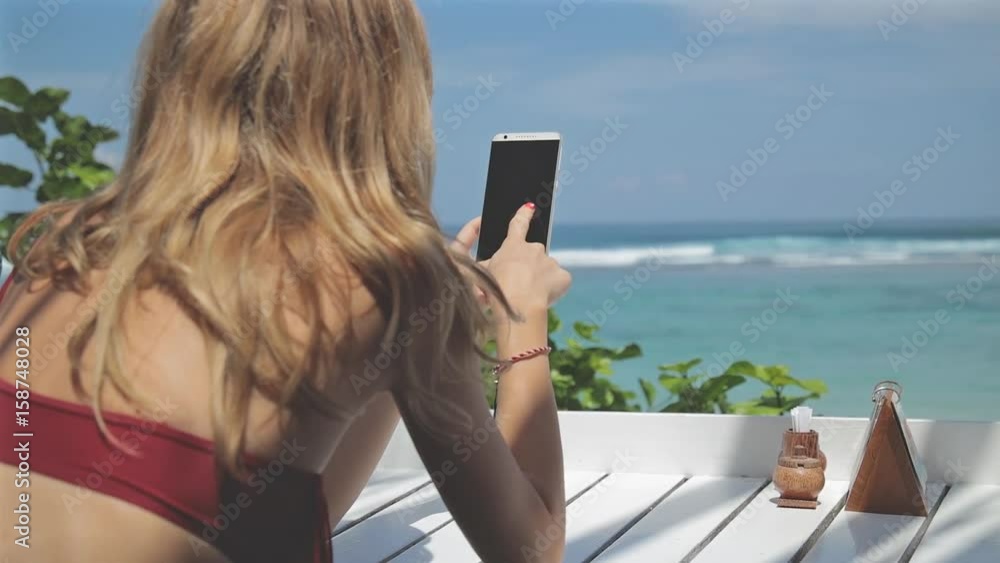 Girl using cellphone in the coffee shop on a tropical exotic beach. Girl using cellphone in the coffee shop on a tropical exotic beach.