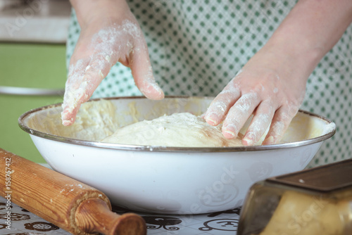 female hands in flour kneading dough in white bowl