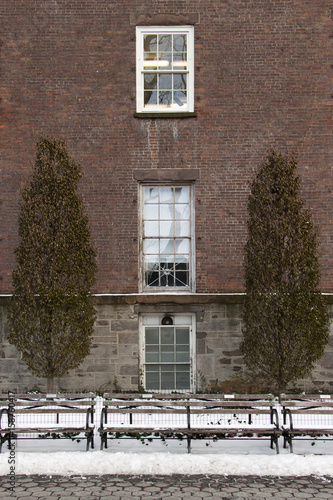 facade of stone and brick with windows, pine trees and benches in a snow day in new york