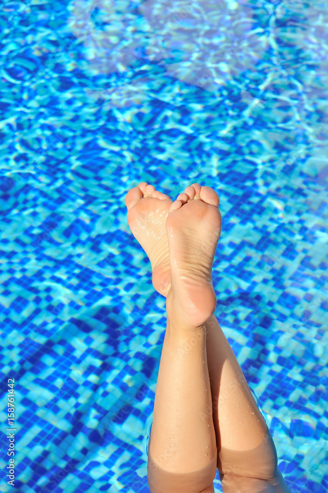 Woman feet in swimming pool on a hot summer day