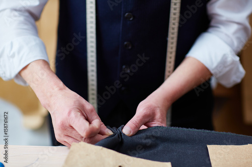 Closeup of skilled tailor working in atelier: pinning and stitching fabric while sewing clothes