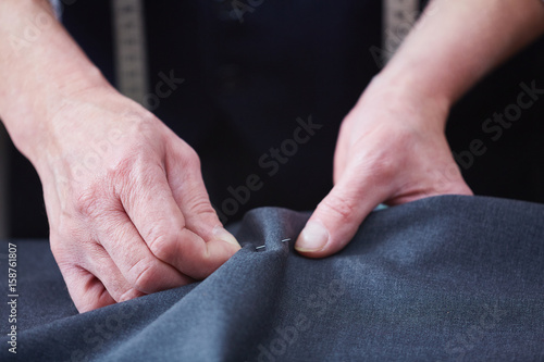 Closeup of unrecognizable skilled tailor working in atelier: hands stitching fabric while sewing clothes on table