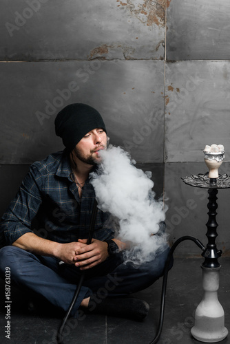 Young handsome bearded man smoking hookah