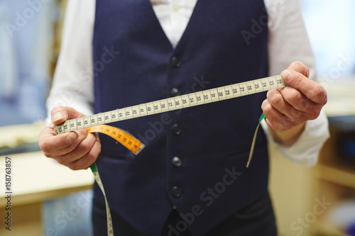 Closeup shot of unrecognizable tailor holding measuring tape in hands while working in traditional atelier studio