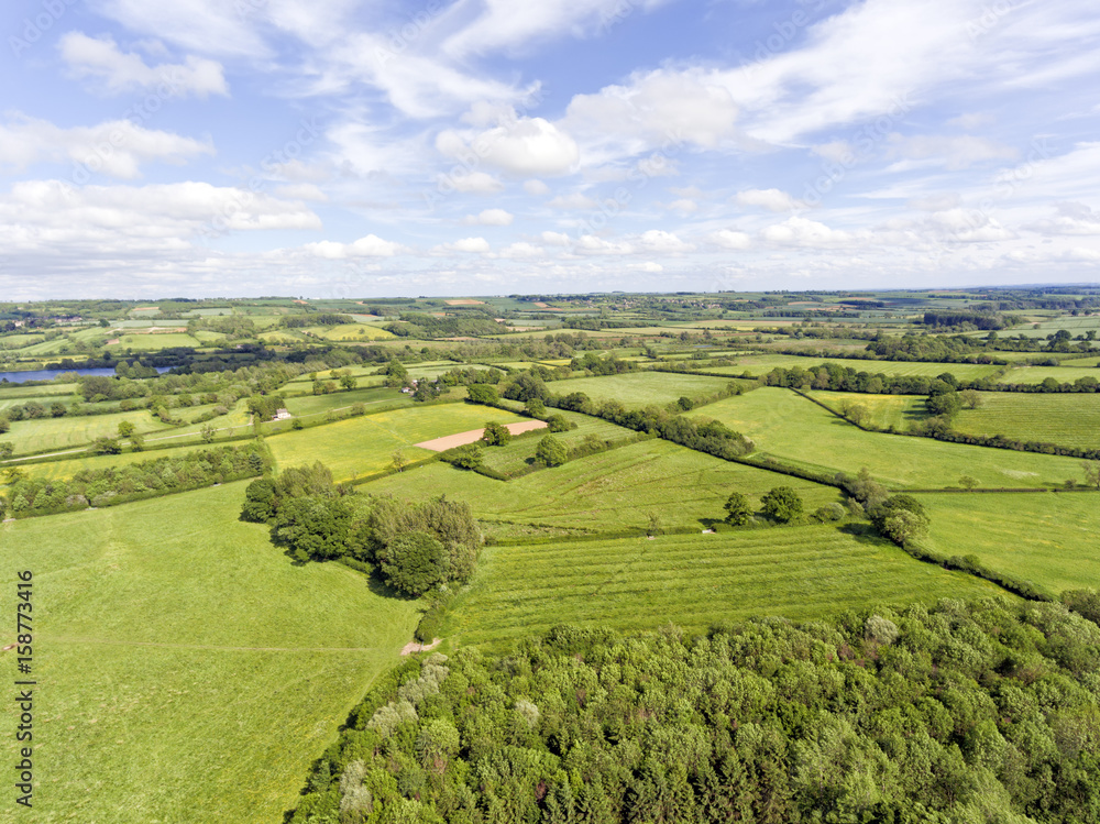 Aerial view of rural english countryside of green farm fields, wildflower meadows, hedgerow, woods, on a summer day .