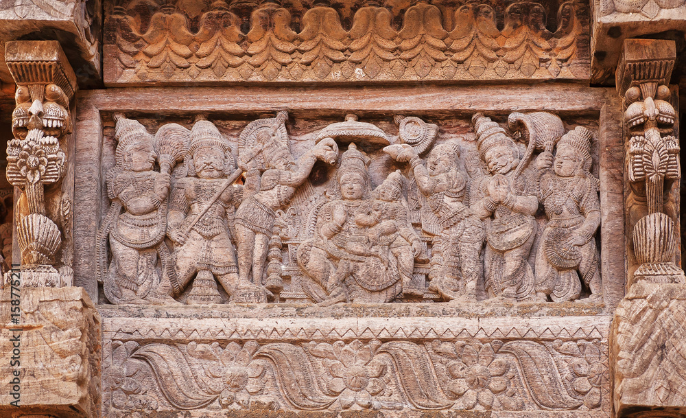 Servants and admirers of the Indian god on carved wooden wall of traditional Hindu temple. Ancient artwork of old religious structure in India