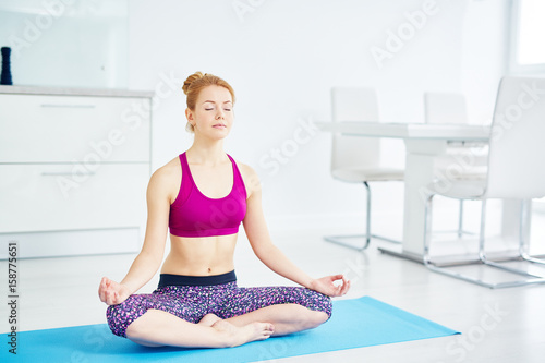 Portrait of fit red haired woman doing yoga at home: sitting in lotus position with eyes closed doing  breathing exercise and relaxing