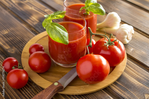 Red tomatoes with tomato juice, garlic and knife on the wooden table