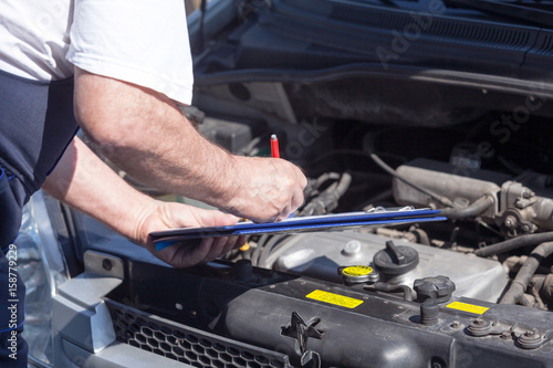 Car or auto mechanic checking a car engine and writing on the clipboard © wellphoto