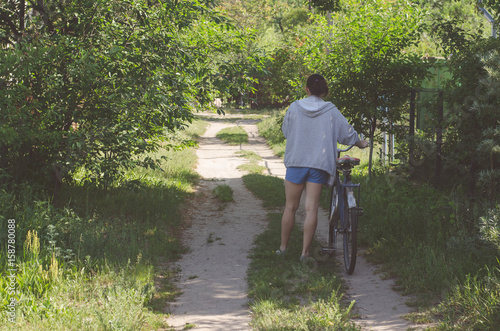 The girl drives an old bicycle on a country road overgrown with grass