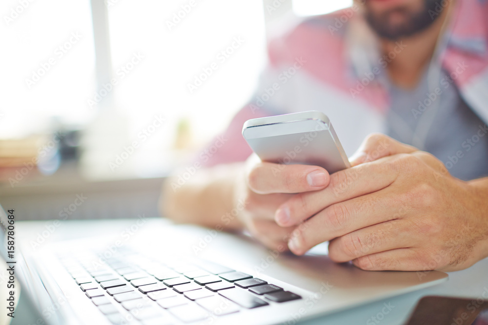Close-up of businessman planning his day with smartphone app, he sitting at table in front of laptop Close-up of businessman planning his day with smartphone app, he sitting at table in front of laptop