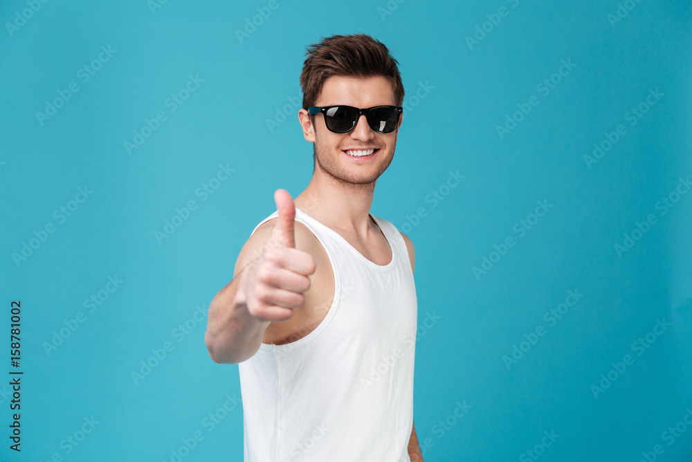 Smiling young guy in sunglasses showing thumbs up Smiling young guy in sunglasses showing thumbs up