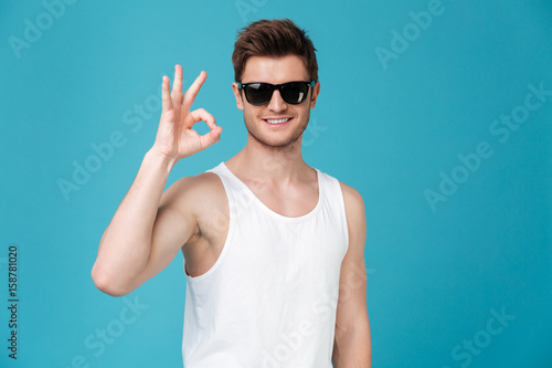 Happy young guy in sunglasses showing okay gesture