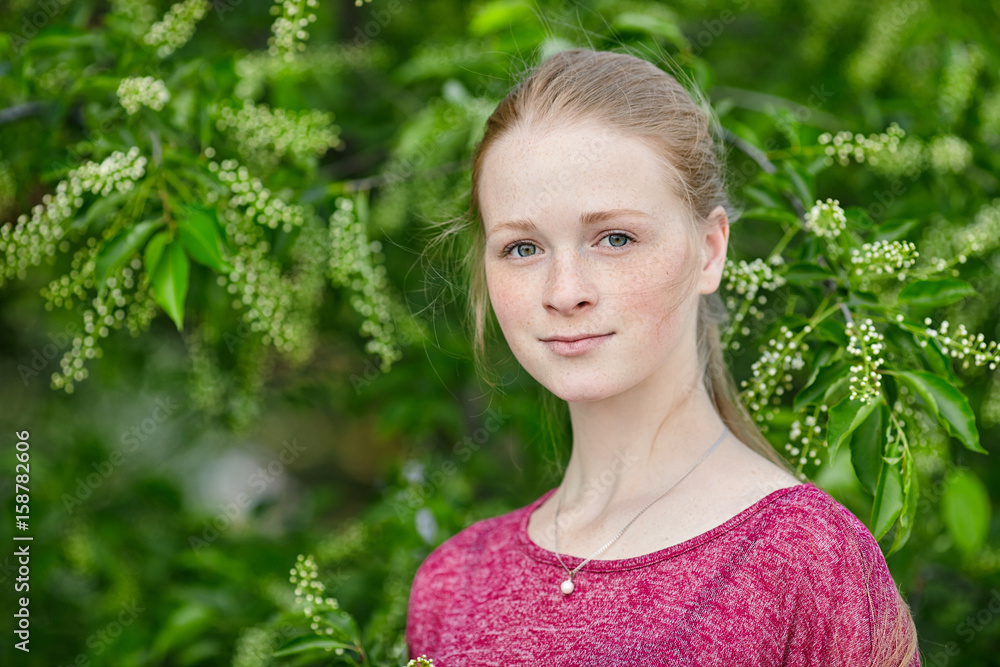 Closeup portrait of young natural beautiful redhead woman in fuchsia blouse posing against blossoming tree with blurred green foliage park background Closeup portrait of young natural beautiful redhead woman in fuchsia blouse posing against blossoming tree with blurred green foliage park background