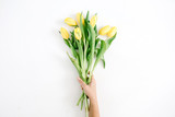 Girl's hands holding beautiful yellow tulip flowers bouquet on white background. Flat lay, top view.