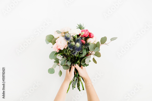 Beautiful flowers bouquet in girls hands: bombastic roses, blue eringium, eucalyptus, isolated on white background. Flat lay, top view. Floral composition photo