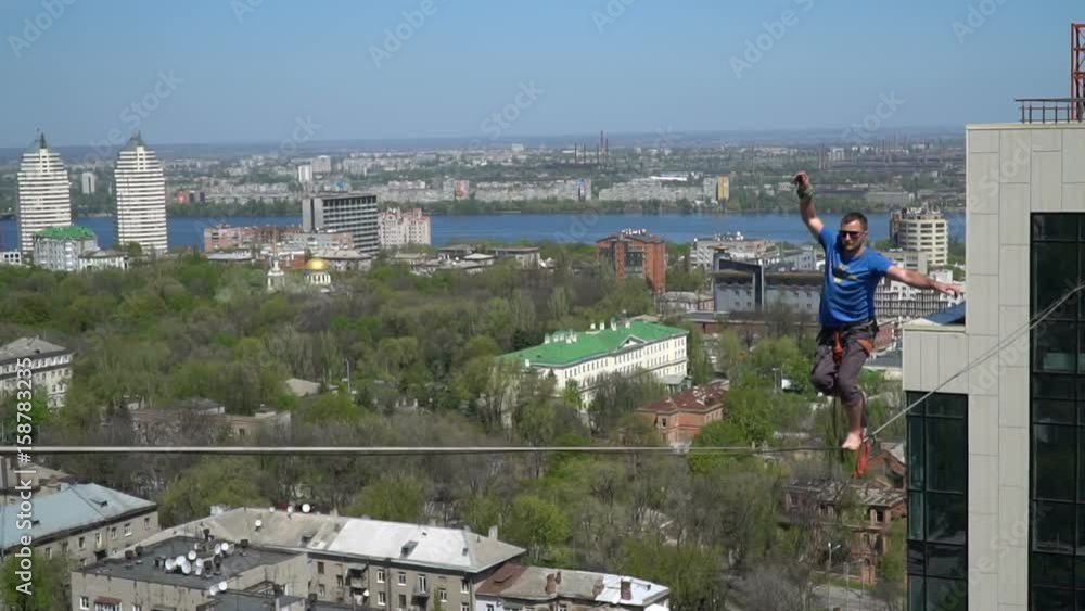 A man in a blue T-shirt gently stands on a tight rope at high altitude A man in a blue T-shirt gently stands on a tight rope at high altitude