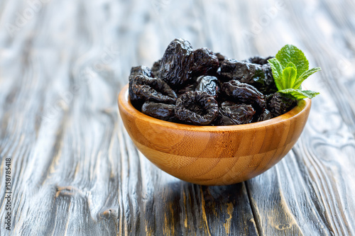 Dried black plums in a wooden bowl.