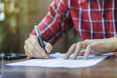 Close-up Of Businessperson Signing Contract,Man writing paper at the desk, man writing with pen and reading books at table,man Signing, Contract, Form..in office ,morning light ,selective focus.