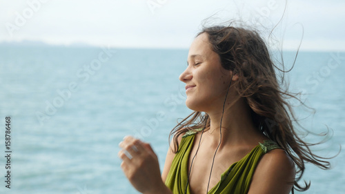 Beautiful dreamy young woman listening to music on headphones on the sailing ship