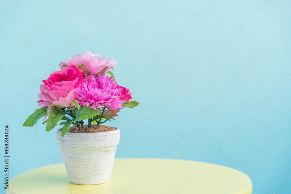 artificial flower pot on wooden table and blue wall background