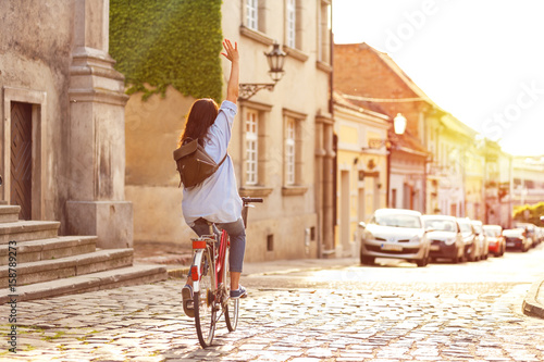 Rear view of young woman riding a bicycle down the street at sunset.