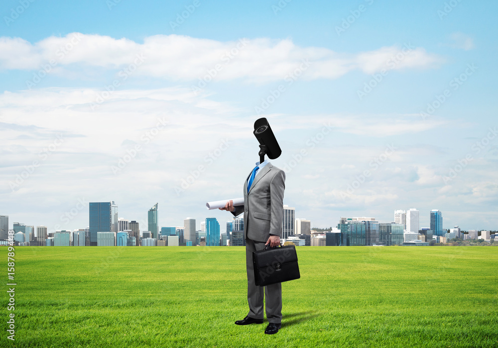 Camera headed man standing on green grass against modern cityscape Camera headed man standing on green grass against modern cityscape