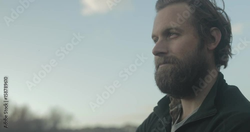 A confident bearded man stands outside