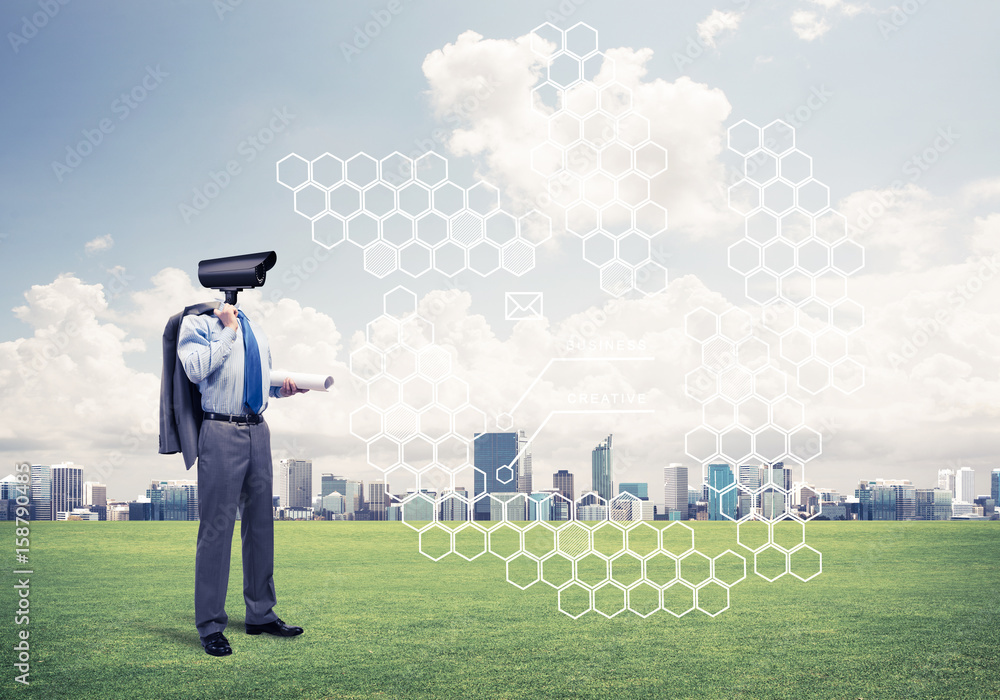 Camera headed man standing on green grass against modern citysca Camera headed man standing on green grass against modern citysca