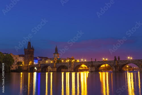 Charles bridge and riverbank with reflections in Prague, Czech republic during sunrise blue hour