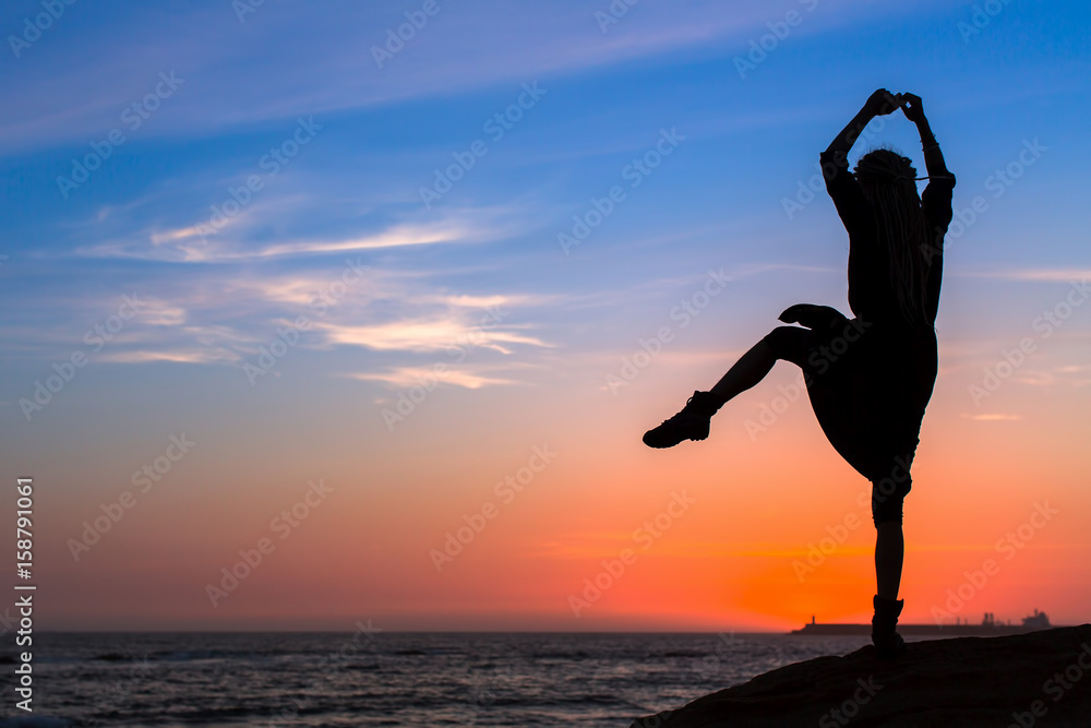 Silhouette of a fun young woman on the sea coast during twilight.