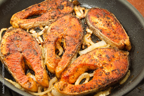 Pieces of trout fried in a frying pan with onions