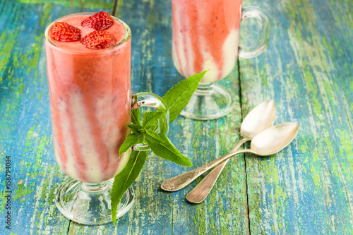 Summer strawberry dessert of a smuza with strawberry and mint in a tall glass on a wooden background photo