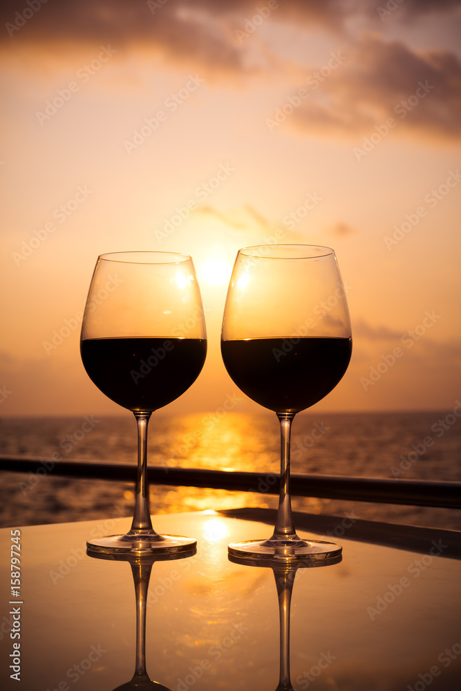 Glasses, red wine and tropical sunset with sea background, nobody.