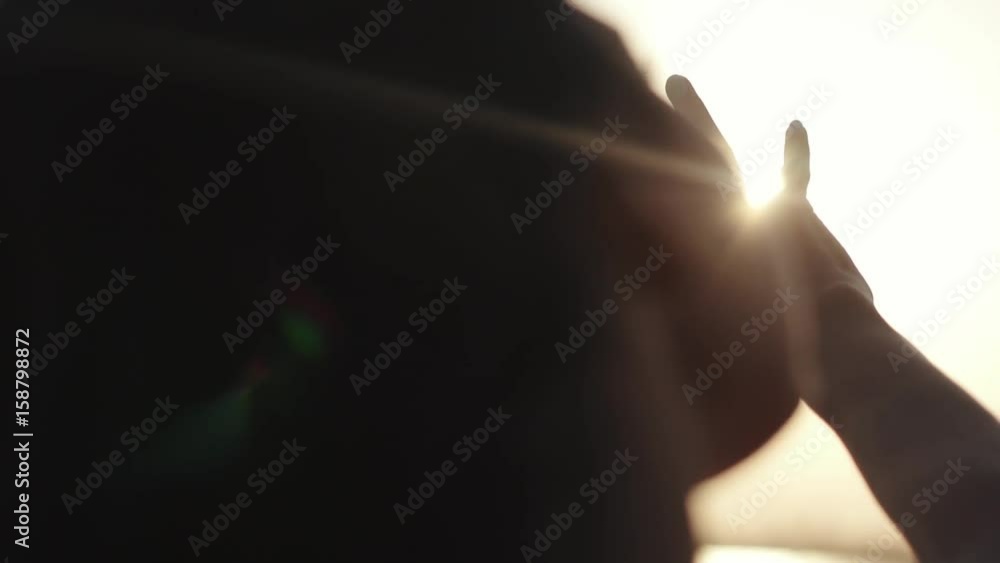 Girl looks at the sun through her hand. girl is resting at sunset. Woman's hand in the sunlight. Waving hand over the sun Girl looks at the sun through her hand. girl is resting at sunset. Woman's hand in the sunlight. Waving hand over the sun