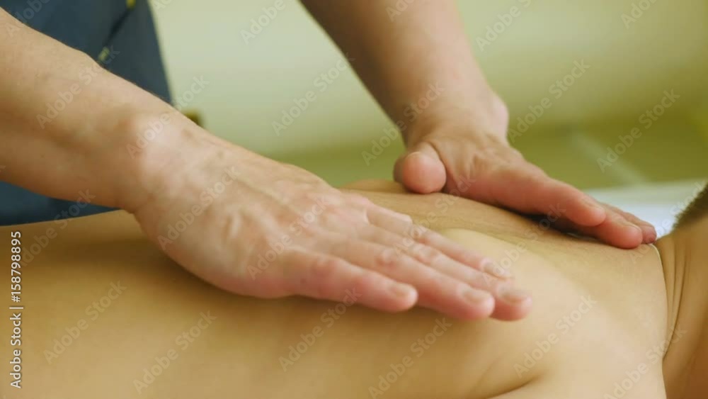 Woman in hospital bathrobe massaging massaging young boy. Pediatric massage Woman in hospital bathrobe massaging massaging young boy. Pediatric massage