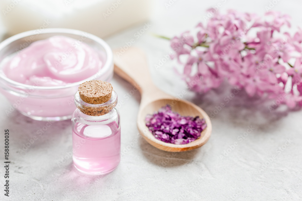 organic salt, cream, extract in lilac cosmetic set with flowers on stone table background organic salt, cream, extract in lilac cosmetic set with flowers on stone table background