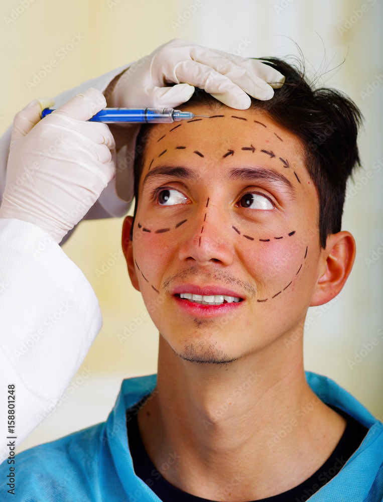 Naklejka premium Closeup of a handsome young man, receiving facial cosmetic treatment injections, doctors hand with glove holding syringe