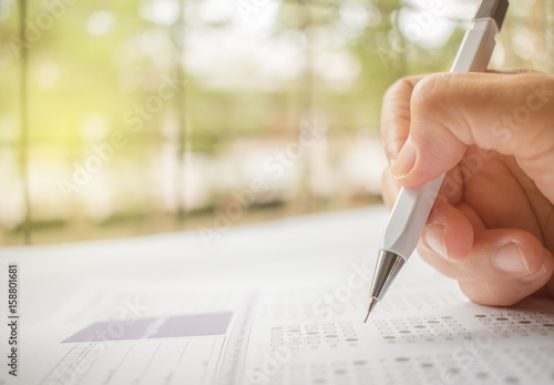 hand student testing in exercise and taking fill in exam carbon paper computer sheet with pencil at school test room, education concept