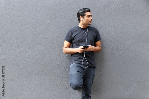 Handsome man wearing black shirt standing against gray wall with phone in hand looking to the side  photo