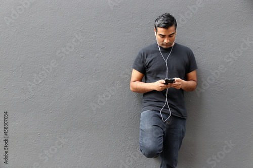 Handsome man wearing black shirt standing against gray wall looking down at phone photo