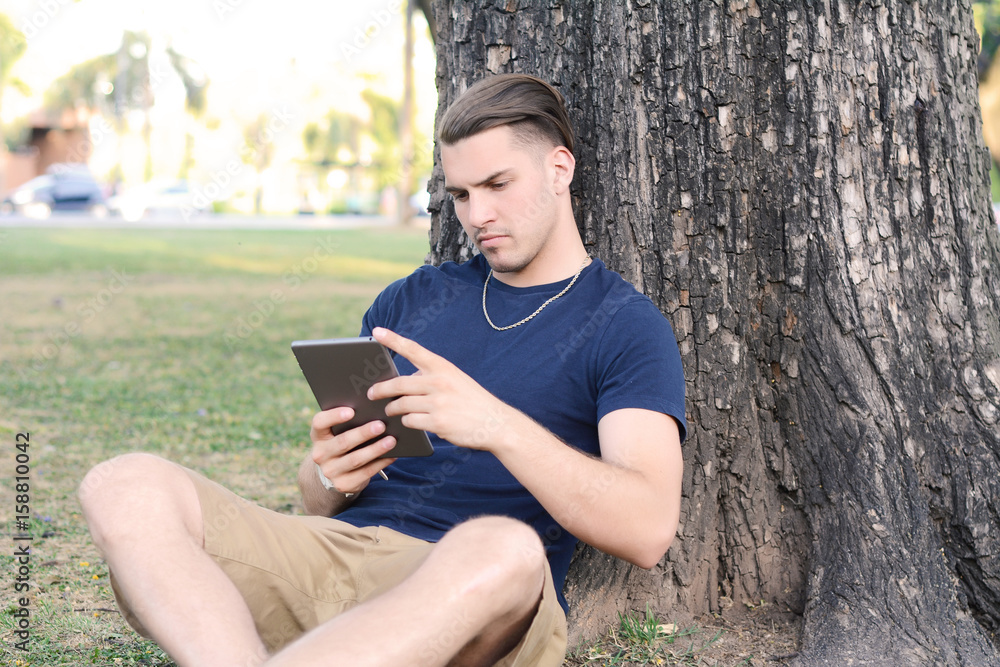 Young man using tablet with headphones in park. Young man using tablet with headphones in park.