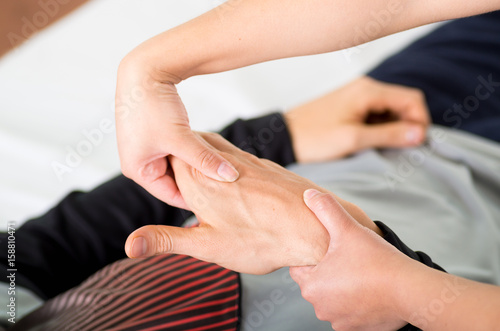 Close up of a massage physiotherapist doing hand massage of a male athlete, in medical office background photo