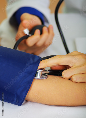 Close up of a young doctor using the stethoscope to hear the pulse while a woman is with a tensiometer in her arm  in a doctor consulting room background