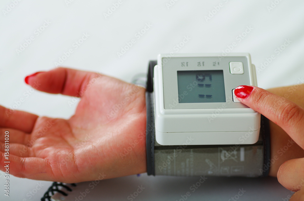Close up of a young patient using an automatic tensiometer in her arm, in a doctor consulting room background Close up of a young patient using an automatic tensiometer in her arm, in a doctor consulting room background