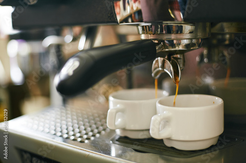 Closeup shot of coffee machine pouring freshly brewed black coffee to porcelain cups